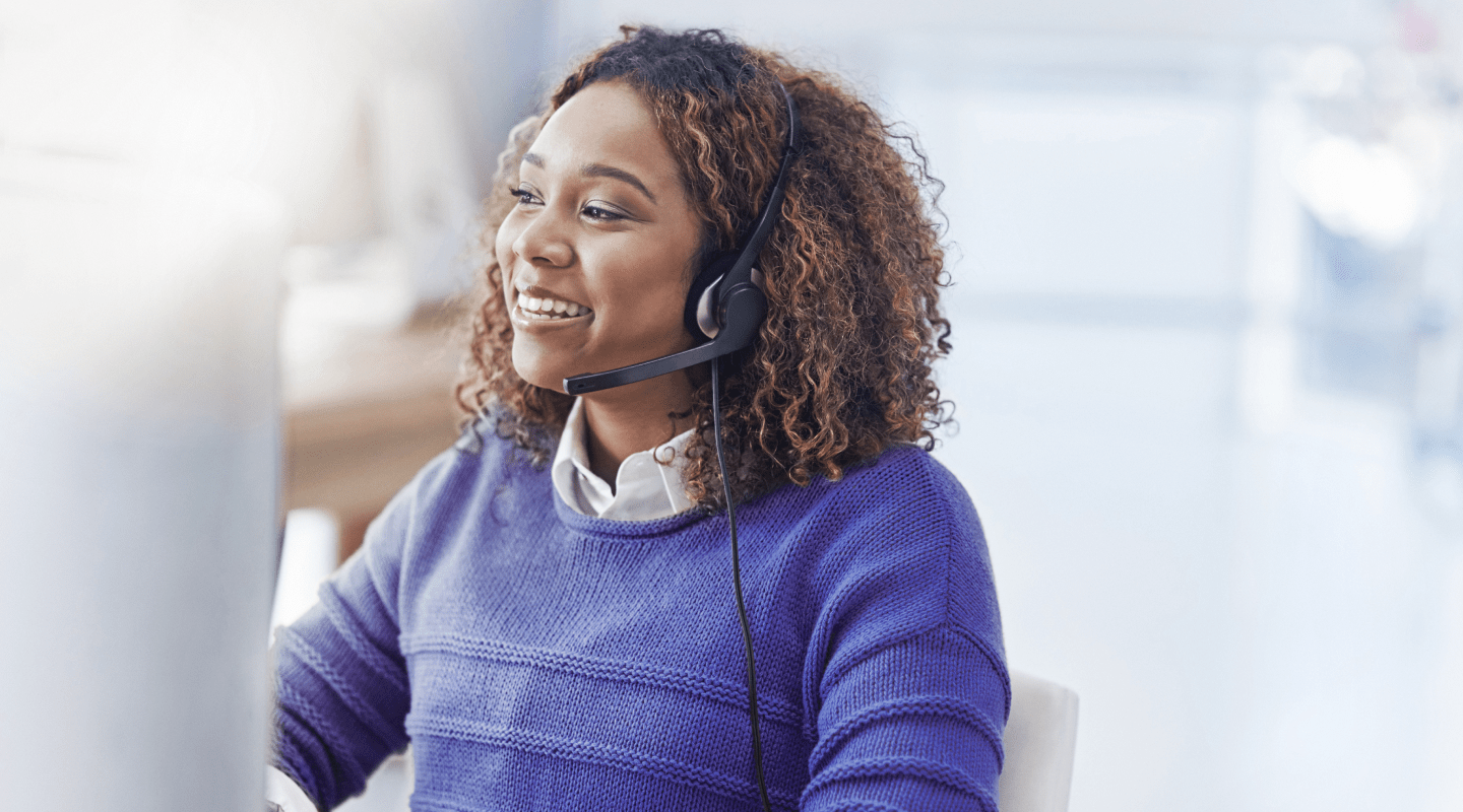 A woman smiles while taking a call on a telephone headset.