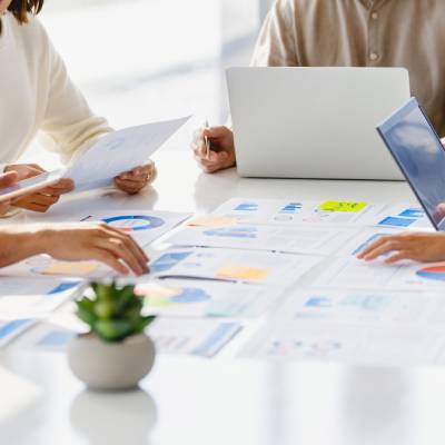 Colleagues working with paperwork on a board room table at a business presentation or seminar. The documents have financial or marketing figures, graphs and charts on them.