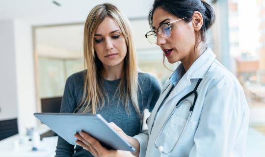 Shot of beautiful female doctor talking while explaining medical treatment with digital tablet to patient in the consultation.