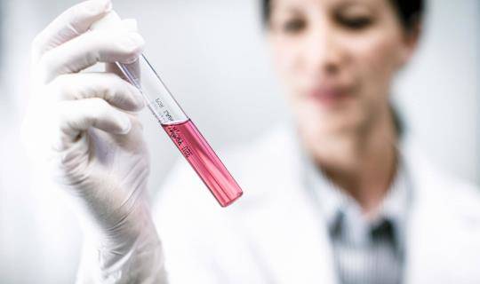 A female scientist examining the contents of a sample tube.