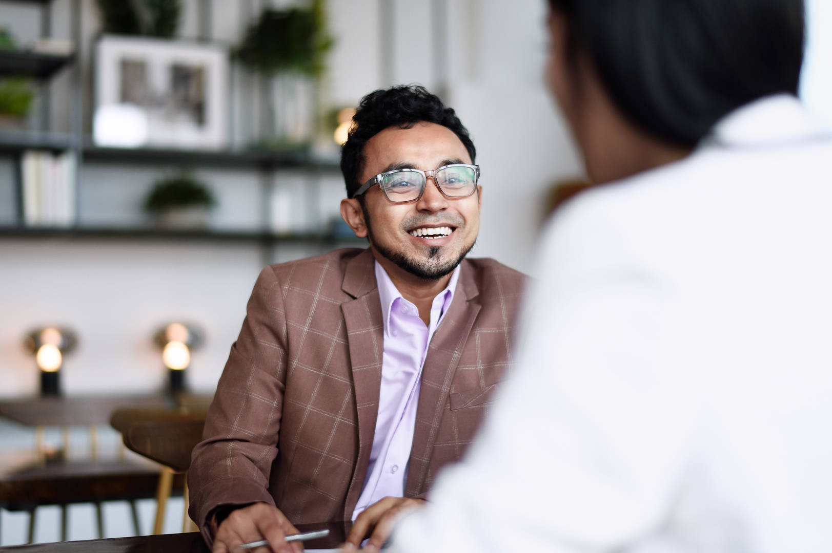 Two people sitting in an office. One of them is facing the camera and smiling
