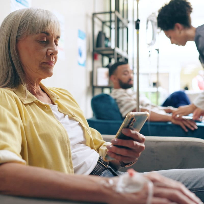 Female patient using her phone while receiving an infusion.