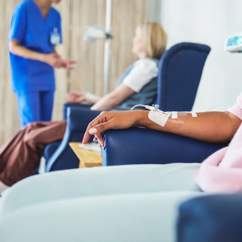 A close up of a patient's arm with a nurse in the background.