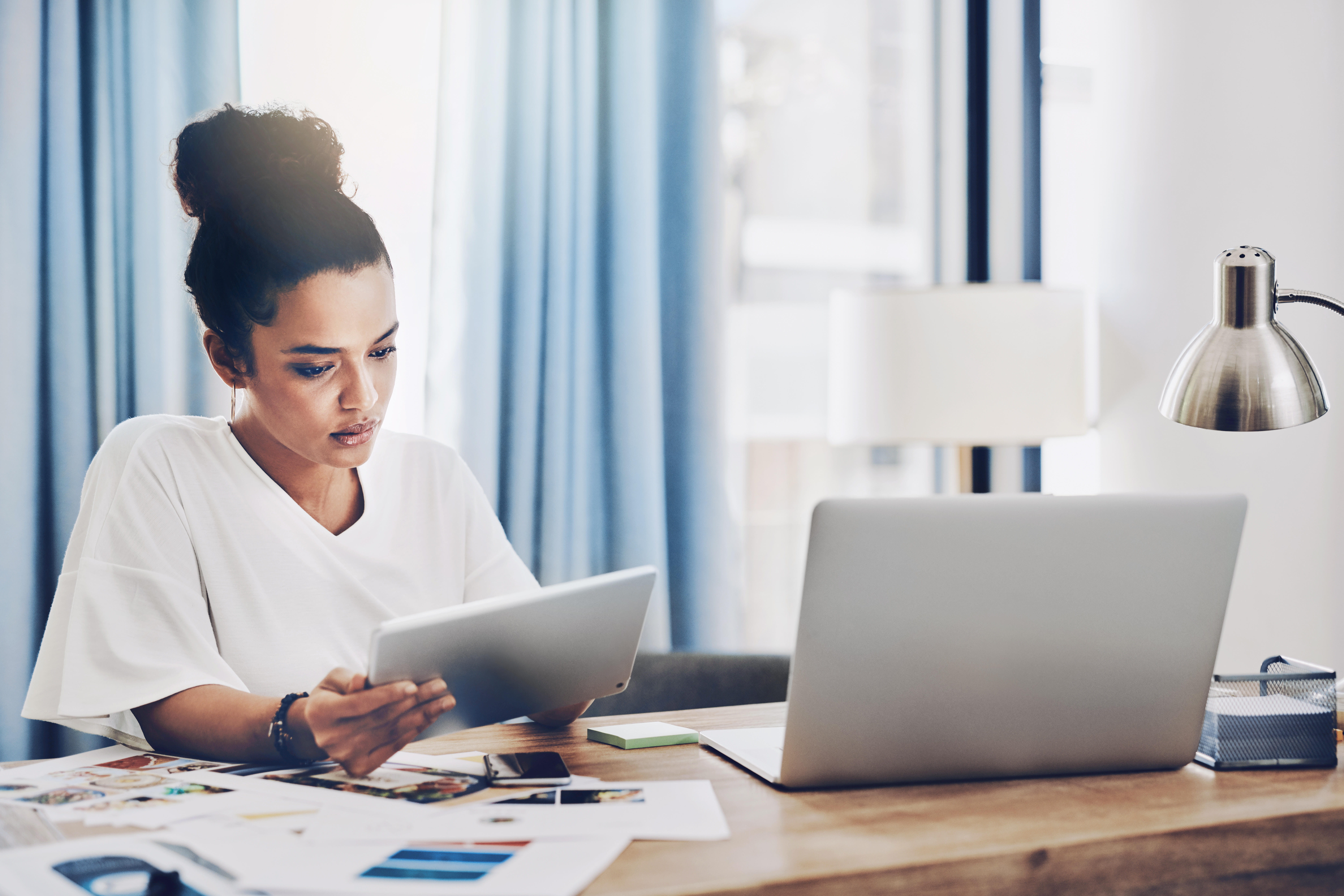 woman looking at tablet with laptop on desk